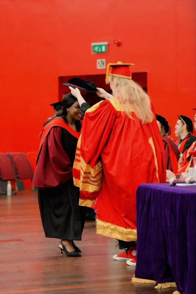 Dr. Alice Maina PhD graduation ceremony at the University of Essex, receiving her doctoral academic cap on stage.